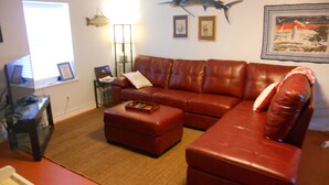 A living room with a brown leather sofa, a coffee table, a fish mounted on the wall, and framed pictures. - Cozy Living Close to the Beach (Bay St Louis)