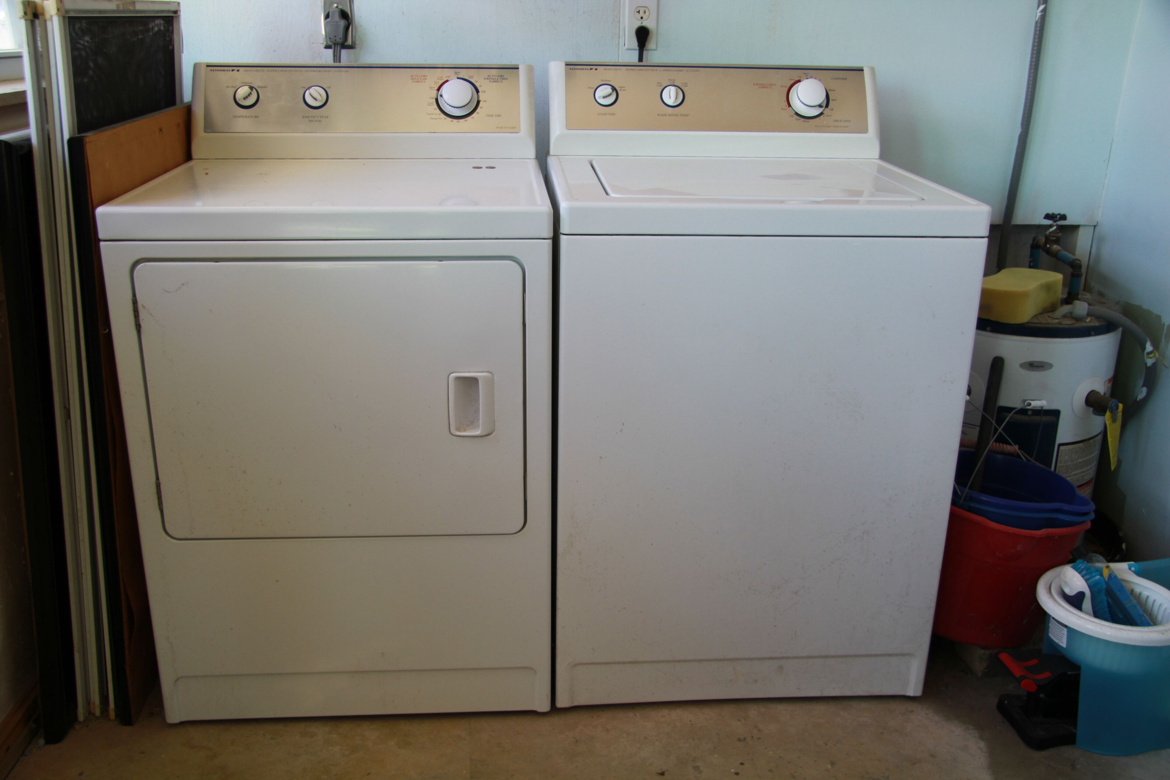 A laundry area with two stacked washing machines, a red bucket, and a blue bucket.
