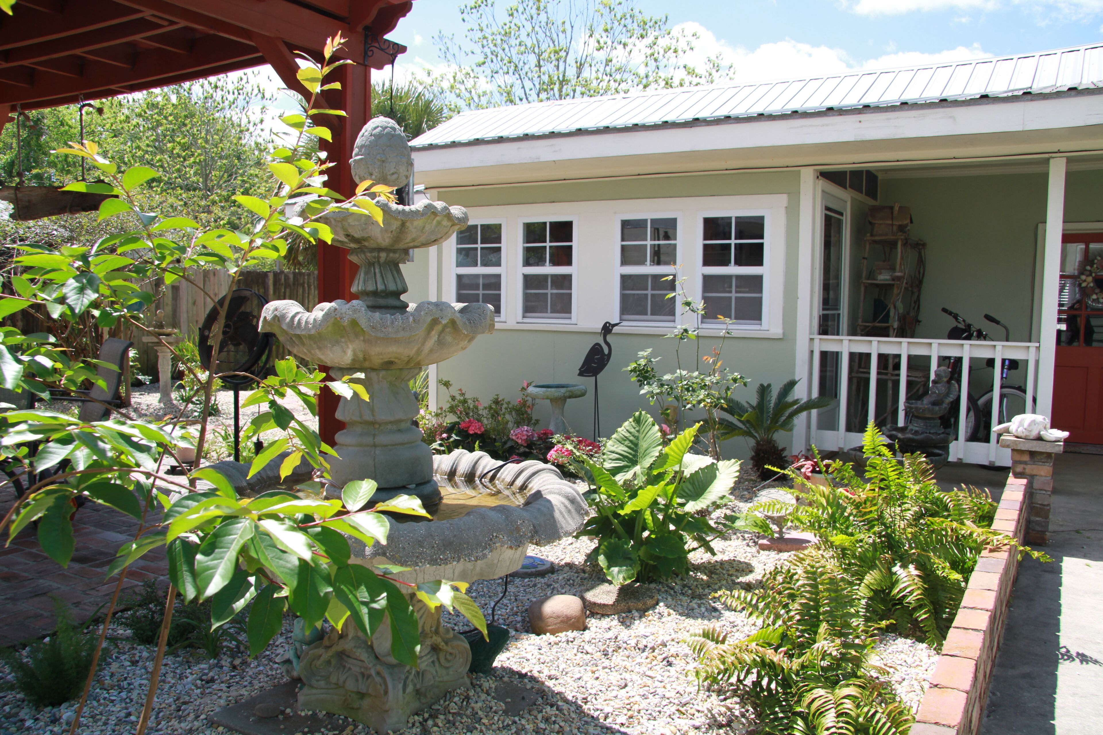 A garden with a stone fountain, various plants, and a building with a porch.