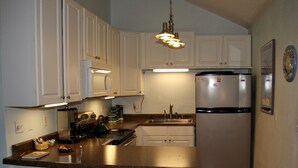 A kitchen with white cabinets, a stainless steel refrigerator, a microwave, and a kettle. - Cozy Living Close to the Beach (Bay St Louis)