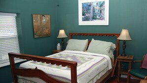 A bedroom with a wooden bed, two bedside tables with lamps, a green wall, and a framed picture above the bed. - Cozy Living Close to the Beach (Bay St Louis)