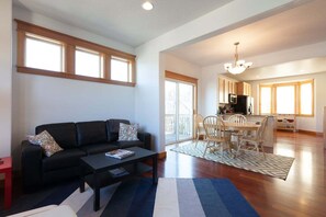 A modern living room with a black sofa, a coffee table, and a dining area with wooden chairs and a table. - Private Reserve - Easy Living, Downtown, Amazing Amenities (Hood River)
