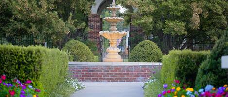 Un jardin agrémenté d’une fontaine, d’une arche en briques et de haies soigneusement taillées.