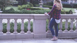 Una persona de pie sobre una barandilla de piedra, contemplando un jardín con una fuente.