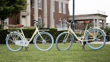 Two vintage bicycles parked on grass with a brick building and a bridge in the background.