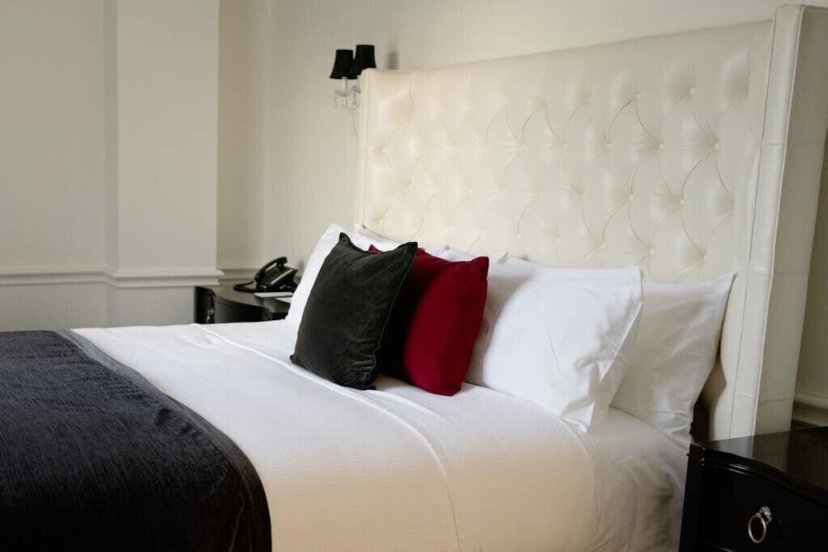 A neatly made bed with a white headboard and a black and red pillow.