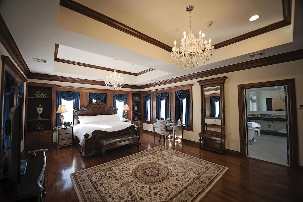 A spacious bedroom with a large bed, a chandelier, and a view of the bathroom.