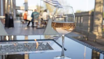Ein Glas Weißwein auf einem Tisch mit Blick auf eine Terrasse und verschwommene Personen im Hintergrund.