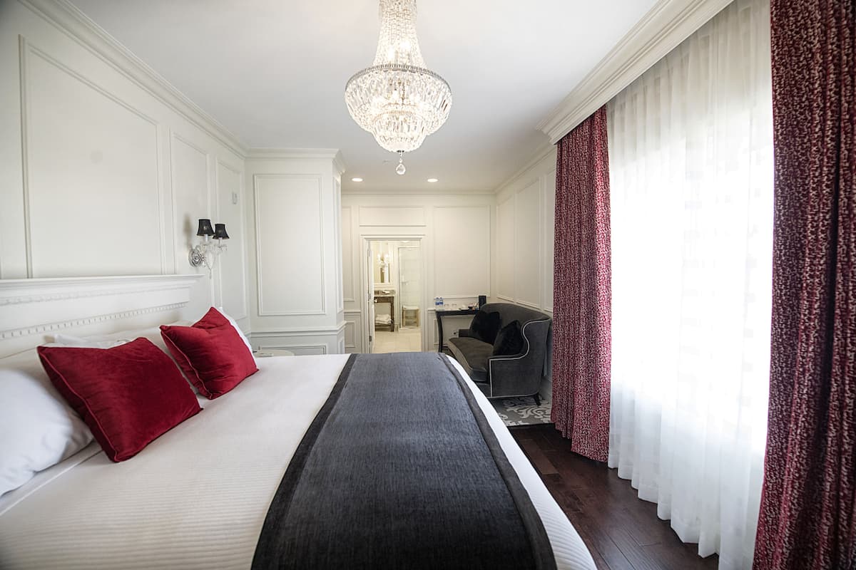A hotel room with a large bed, a chandelier, a desk, and a view of the hallway.