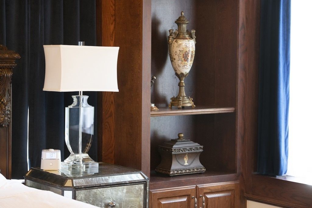 A hotel room with a bed, a nightstand with a lamp, a decorative vase, and a wooden cabinet.