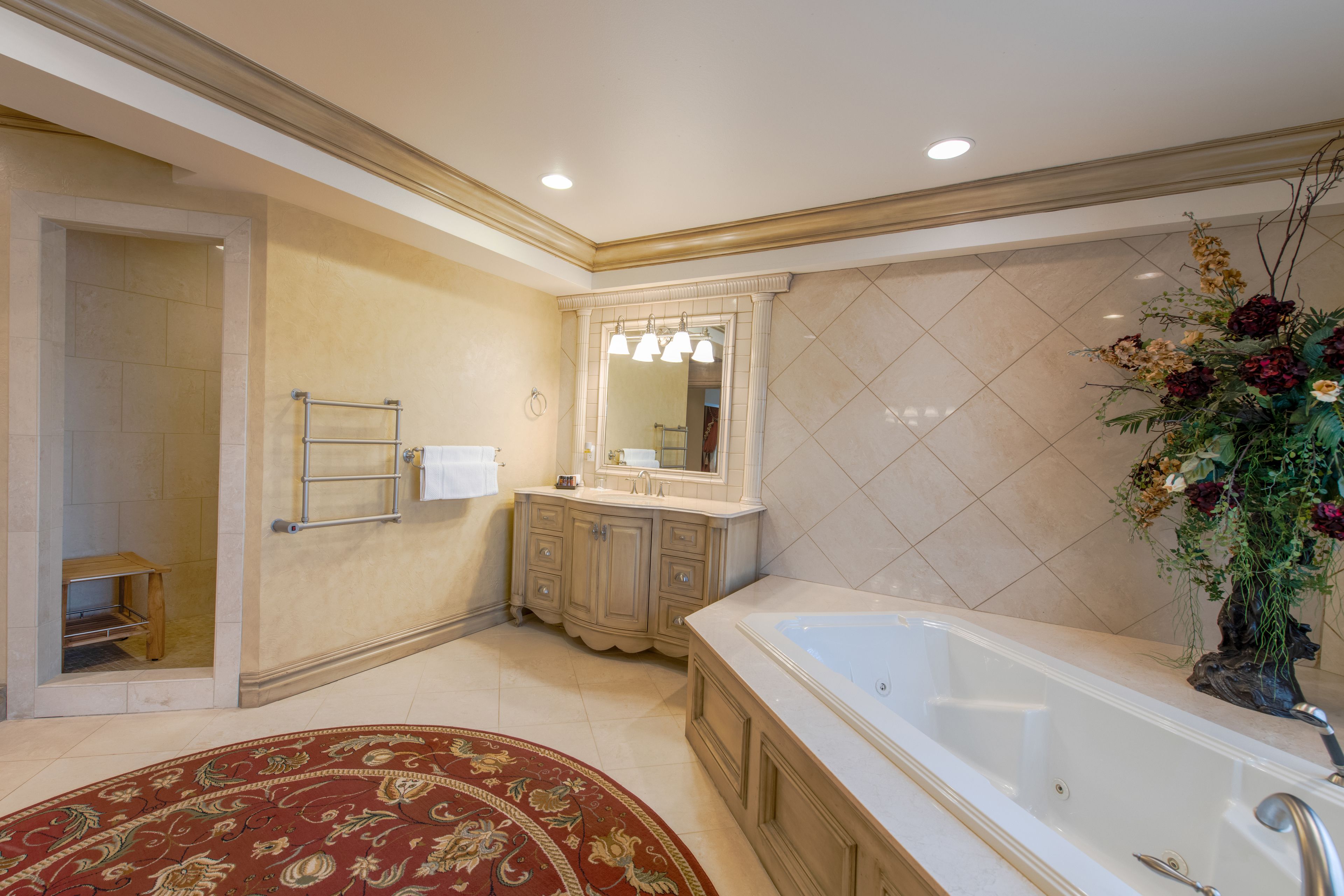 A spacious bathroom with a large bathtub, a vanity with a mirror, and a decorative plant.