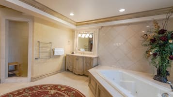 Une salle de bain spacieuse avec une grande baignoire, un meuble-lavabo avec un miroir et une plante décorative.