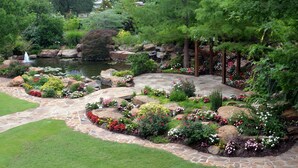 Un jardín ajardinado con un estanque, un sendero de piedra y diversas plantas y flores.