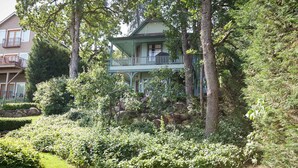 Een twee verdiepingen tellend huis met een balkon, omgeven door weelderige begroeiing en bomen.