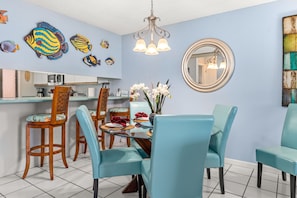 A dining area with a round glass table, blue chairs, and a vase of white flowers.