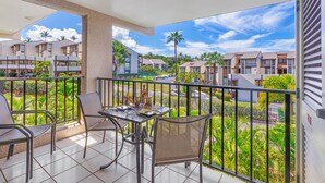 Een balkon met een tafel en stoelen, met uitzicht op een woongebied met palmbomen en huizen.