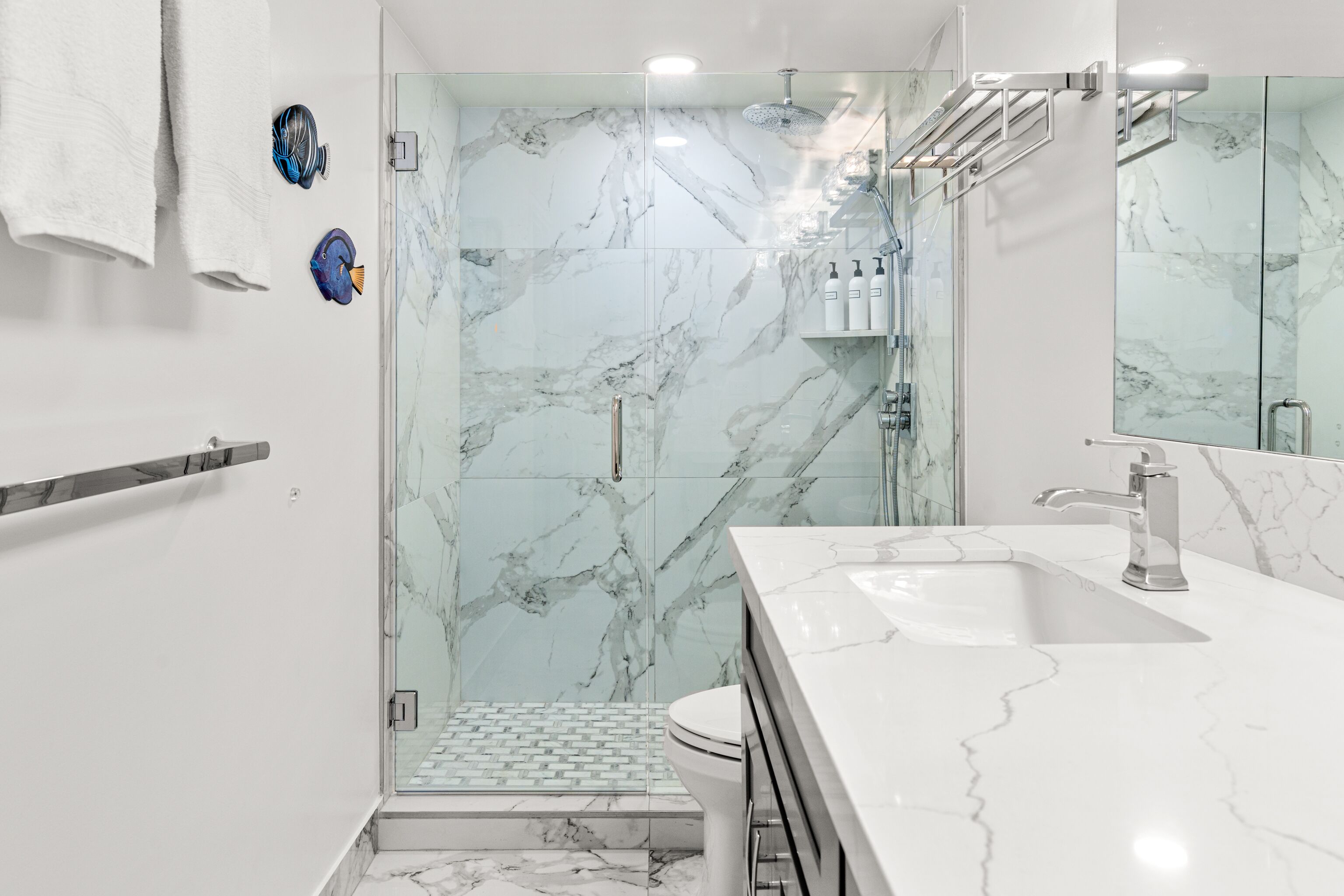 Une salle de bain moderne dotée d’une douche à parois de verre, d’un lavabo en marbre blanc et d’une porte en verre donnant accès à une zone de douche carrelée.