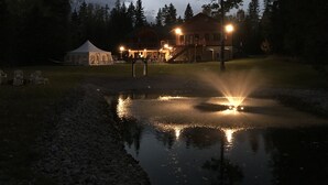 Järvenrantainen mökki, jossa on peilimäinen lampi, teltta ja useita valoja sisältävä rakennus.