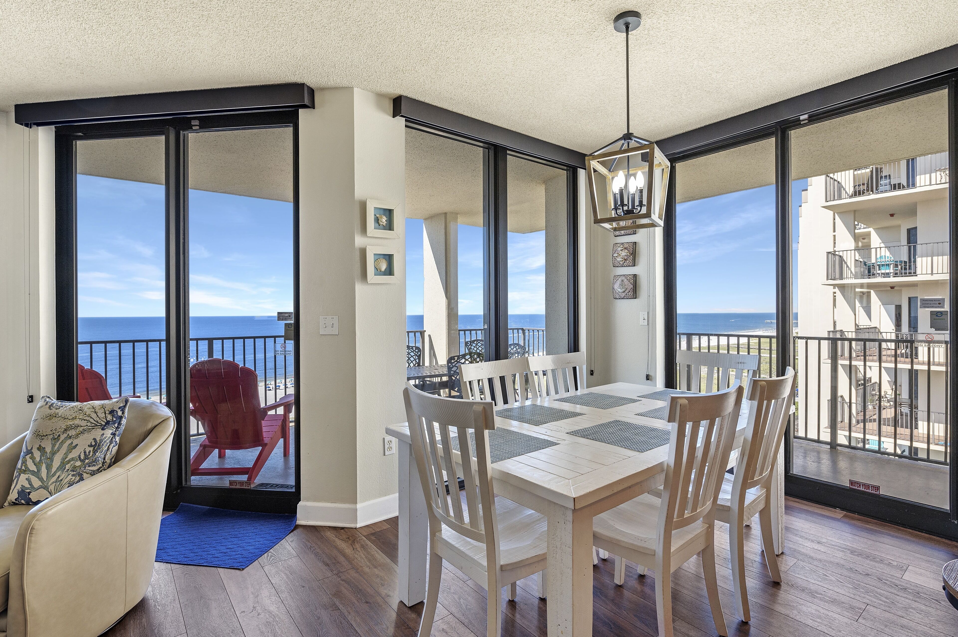 A dining area with a table and chairs, a sofa, and a view of the ocean through large sliding glass doors.