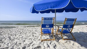 Two beach chairs under a blue umbrella on a sandy beach with the ocean in the background. - Phoenix 8 1101 | Beachfront View | Spacious Corner Condo | My Beach Getaways (Orange Beach)