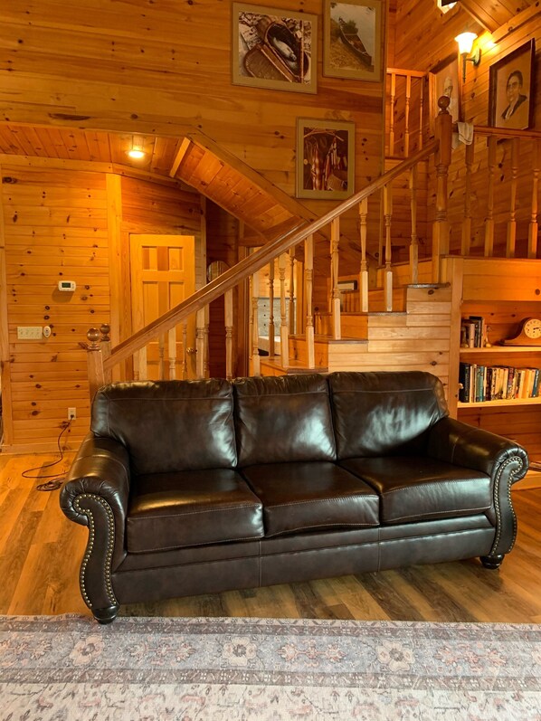 A wooden interior with a leather sofa, a staircase, and a bookshelf.
