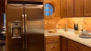 Eine Küche mit Holzschränken, einem Edelstahlkühlschrank, einem Wasserspender und einem Fenster mit Blick auf Bäume.