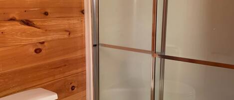 A wooden cabin bathroom with a glass-enclosed shower and a white toilet.