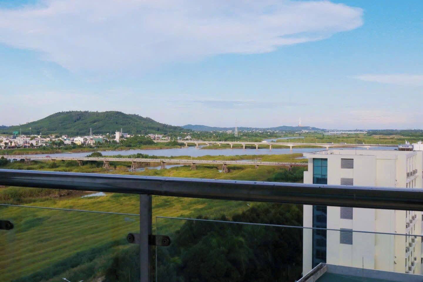 A view from a balcony overlooking a river with bridges, a hill, and buildings in the distance.