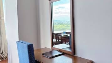 Un escritorio de madera con un espejo, una silla azul y vistas a un paisaje por la ventana.