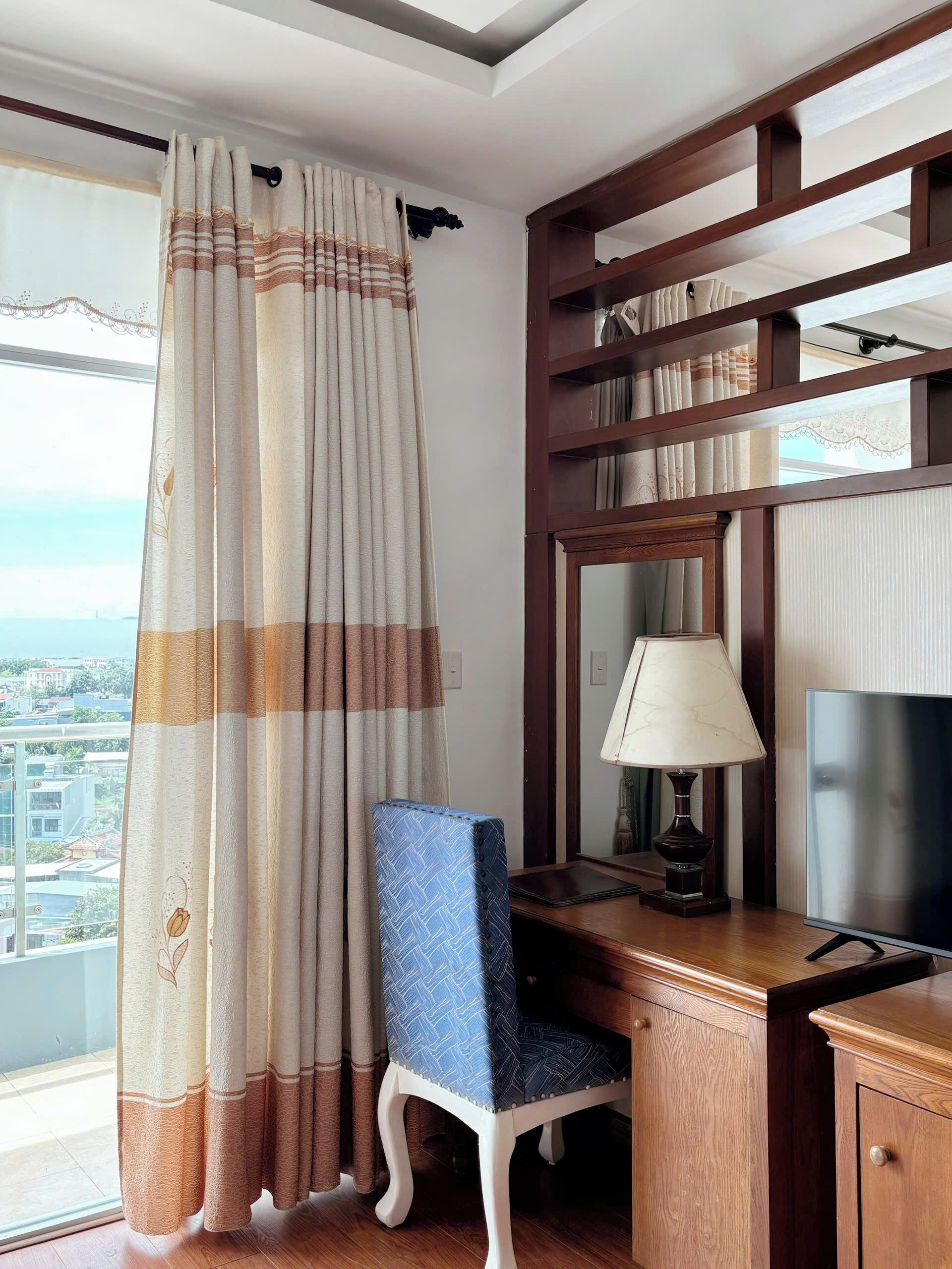 A hotel room with a desk, chair, and a large window with curtains.