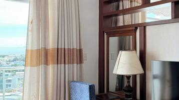A hotel room with a desk, chair, and a large window with curtains.