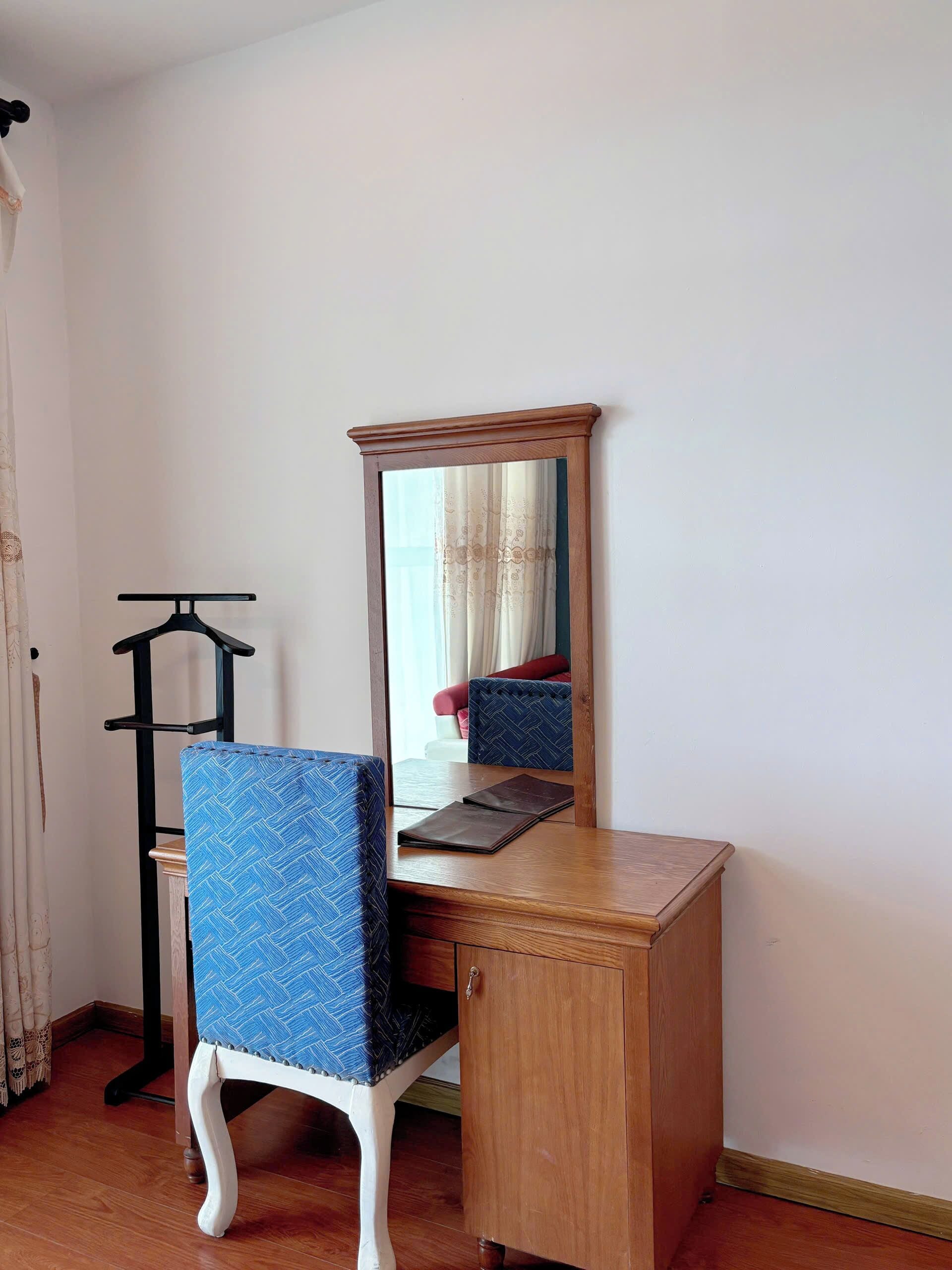 Een houten bureau met een spiegel, een blauwe stoel en een zwarte kapstok.