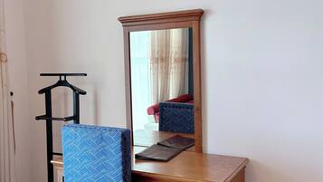 Een houten bureau met een spiegel, een blauwe stoel en een zwarte kapstok.