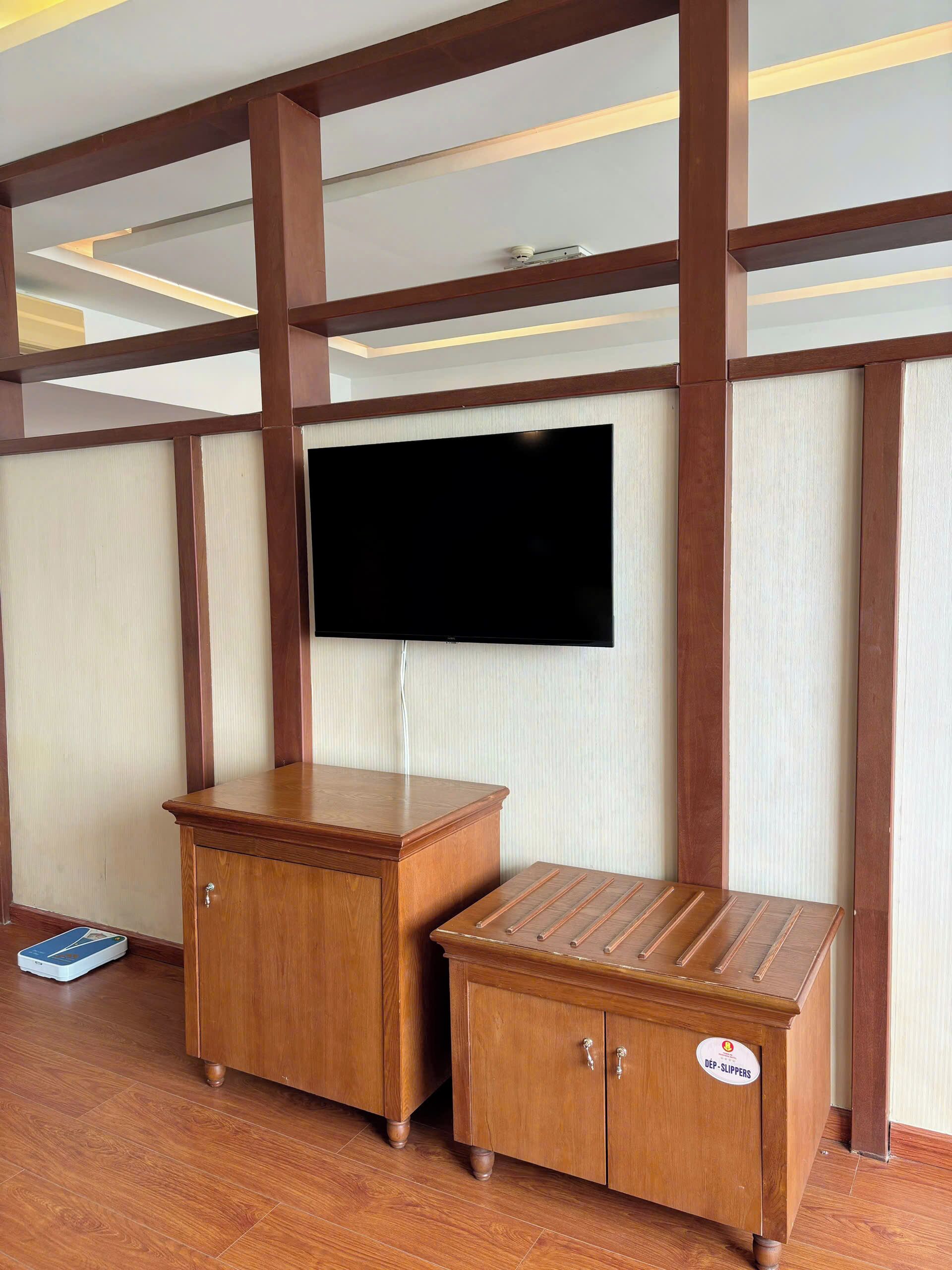 A room with a wooden cabinet, a television mounted on the wall, and a small wooden stool.