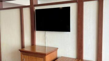 A room with a wooden cabinet, a television mounted on the wall, and a small wooden stool.
