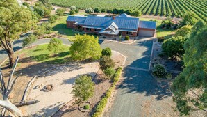 Une grande maison avec un garage, entourée d’une pelouse bien entretenue et d’un vignoble en arrière-plan.
