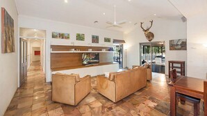 Un vaste espace de vie au design moderne, comprenant un meuble de rangement en bois pour les appareils multimédias, des canapés en cuir et une tête de cerf fixée au mur.