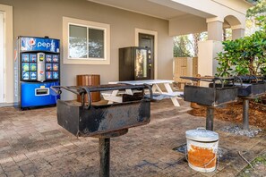 An outdoor patio area with a Pepsi vending machine, a wooden bench, and barbecue grills. - GREAT LOCATION ~ Luxury End-Unit Condo, Walk 2 Beach, Pool, Hot Tub,  FREE Activities!! (Miramar Beach)