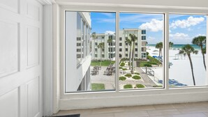 Uitzicht vanuit een raam op een strandhotel met zwembad en palmbomen.