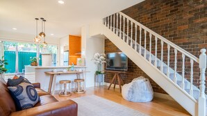 A living room with a brown leather sofa, wooden coffee table, and a white rug. A staircase with white balusters leads to a brick wall. - Buckingham Pet friendly (Richmond)