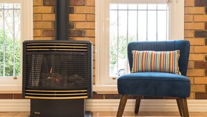 A room with a wood-burning stove, a blue chair with a striped cushion, and a brick wall. - Buckingham Pet friendly (Richmond)