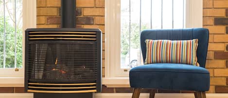 Une pièce avec un poêle à bois, une chaise bleue avec un coussin rayé et un mur en briques.
