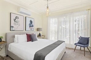 Un dormitorio con una cama grande, una mesita de noche con lámpara, una silla y dos obras de arte colgadas en la pared.