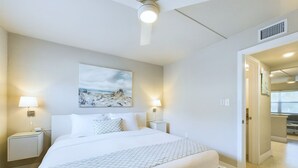 Une chambre d’hôtel avec un lit, deux lampes de chevet, un ventilateur de plafond et un tableau au mur.
