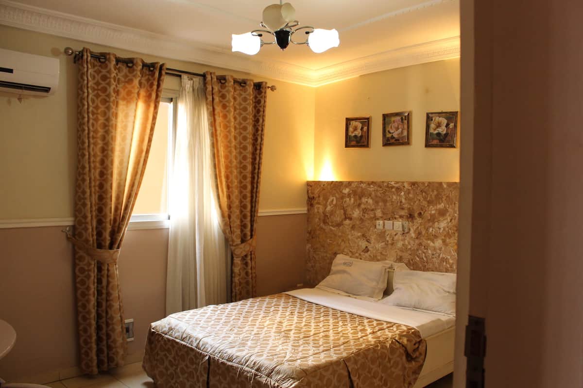 A bedroom with a bed, curtains, a ceiling fan, and wall-mounted artwork.