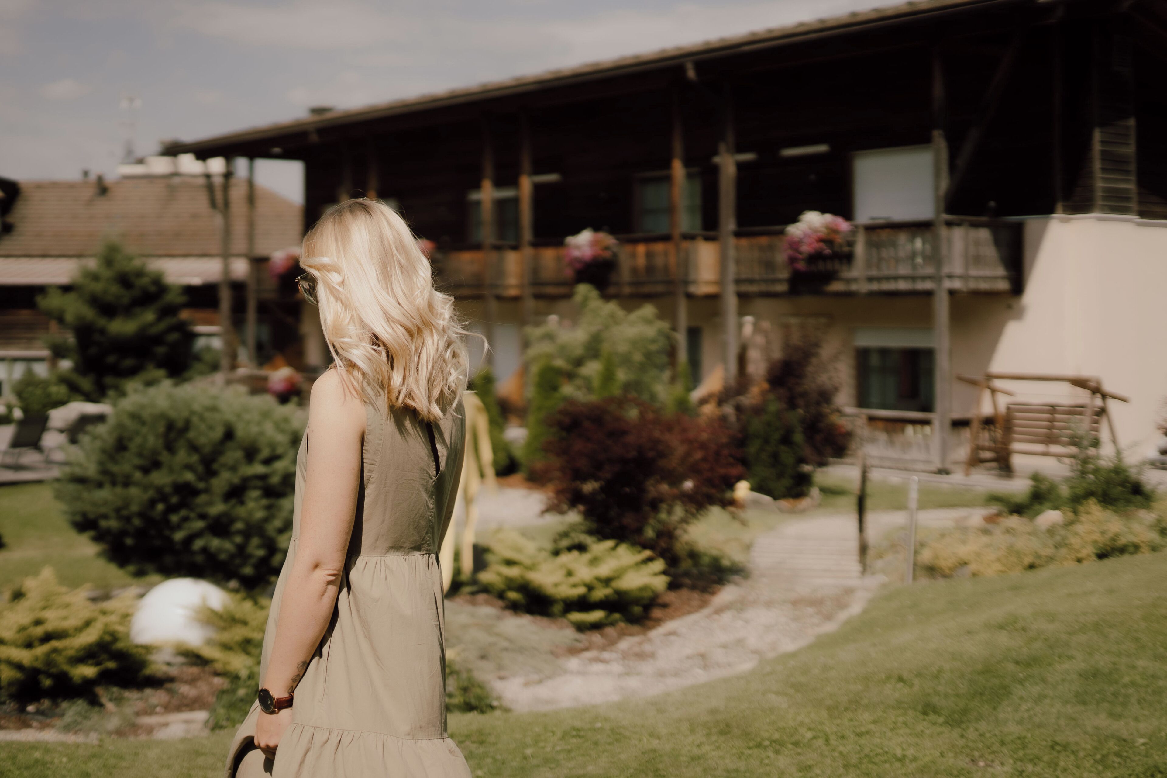 A woman in a dress standing in a garden with a building in the background.