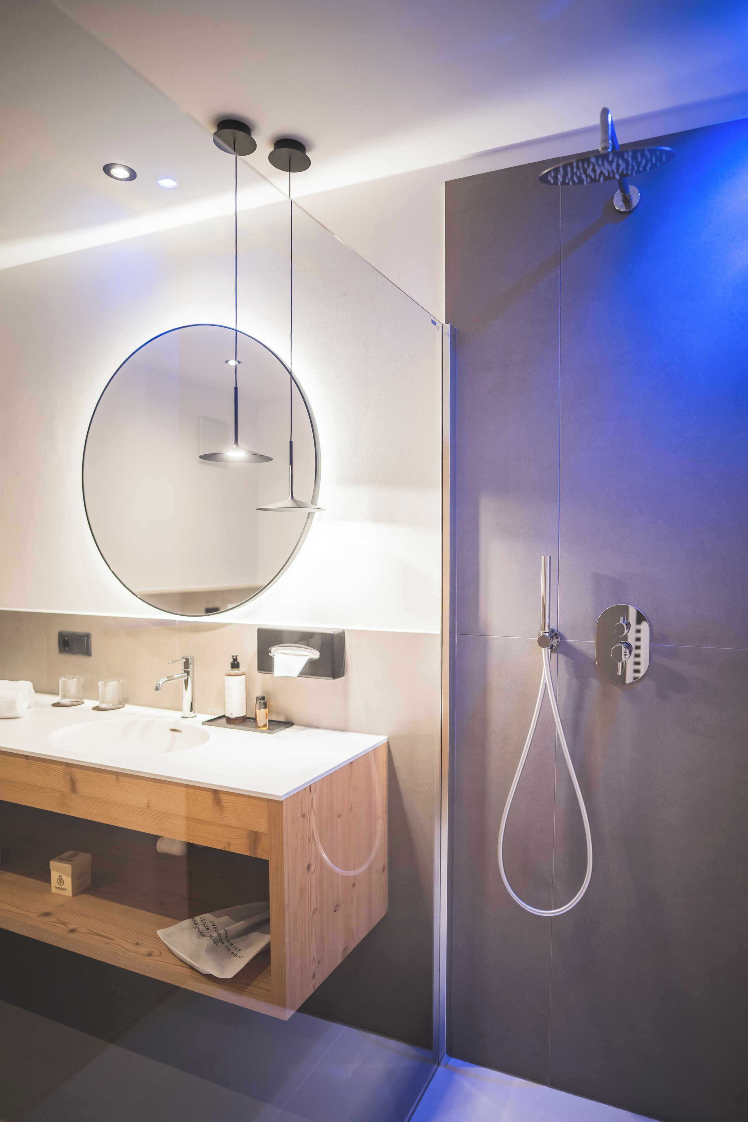 A modern bathroom with a wooden vanity, a large mirror, and a walk-in shower.