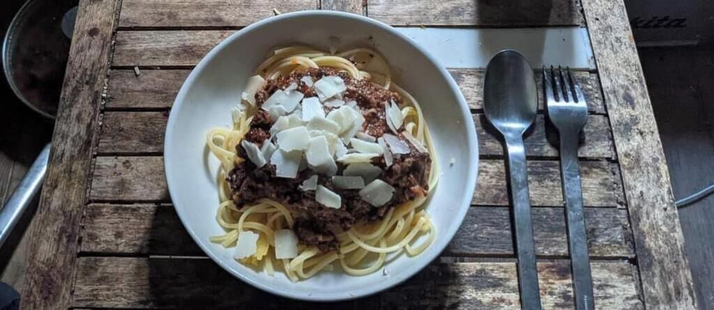 Un plato de pasta con carne y queso sobre una mesa de madera.
