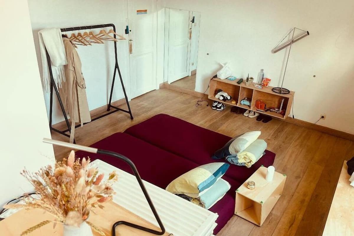 Una habitación con una cama, un aparador de madera, un perchero y una lámpara de pie.