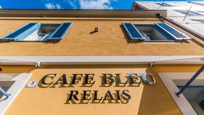 A building facade with the sign "CAFE BLEU RELAIS" and two windows with blue shutters. - Cafe Bleu Relais (Sassari)